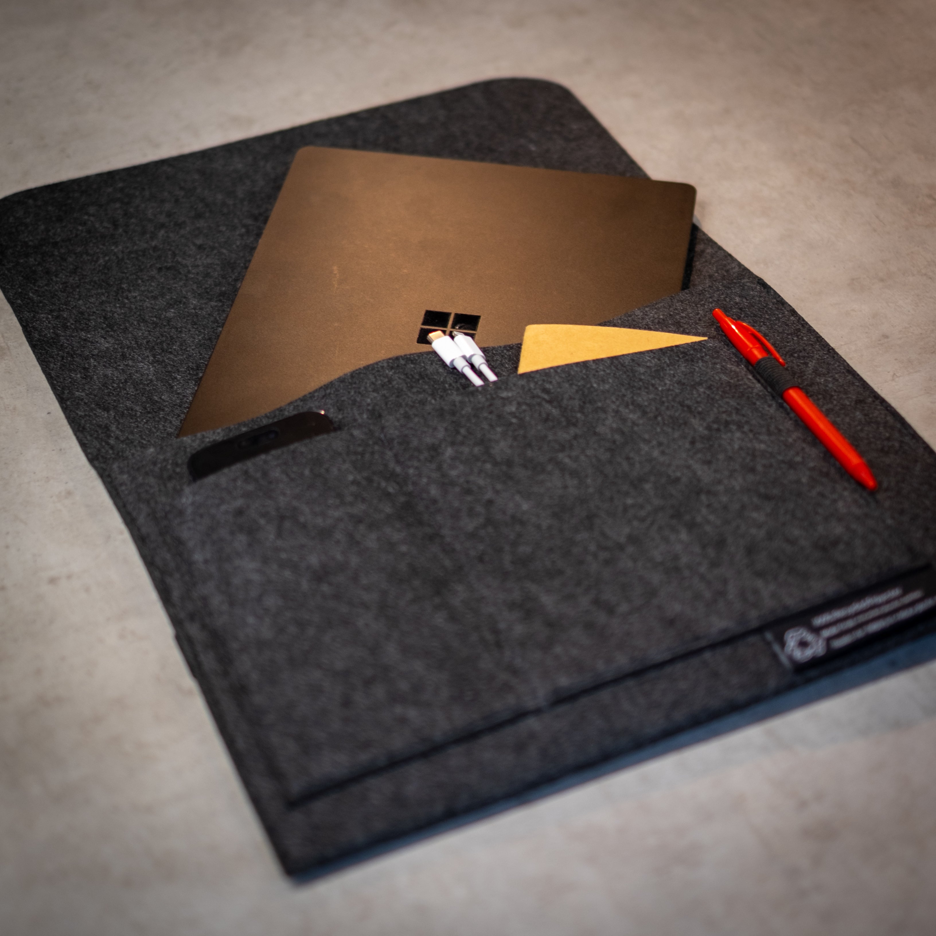 RMIT Store rPET Utility Laptop Sleeve in charcoal grey felt, made from 100% recycled polyester, featuring multiple organiser pockets for a laptop, phone, cards, cables, and pen, with an eco-label stitched on the front for sustainability branding.